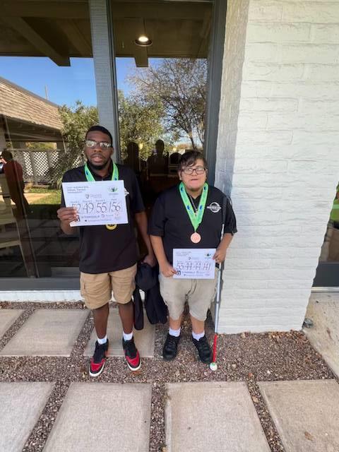 George and Tierece hold the certificates they earned at the golf tournament and smile at the camera.